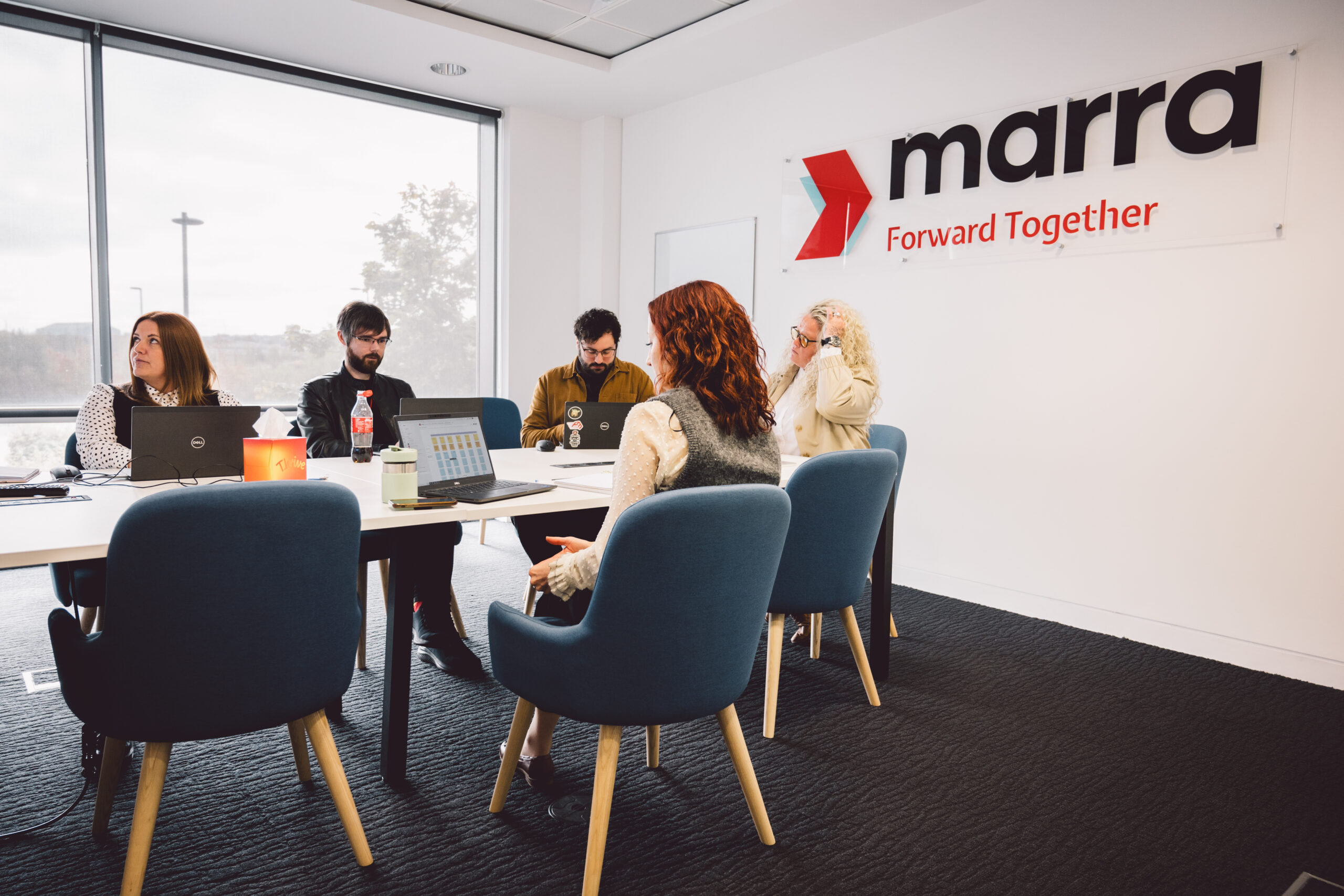 five people sat round a table with laptops looking at a screen which is out of shot.