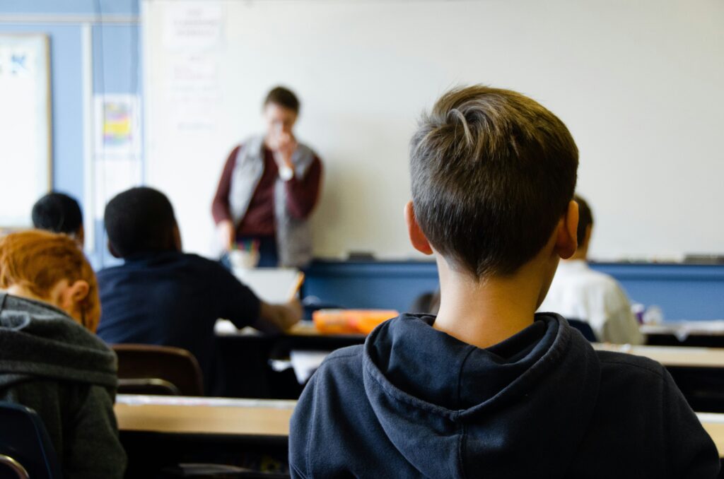 Picture from the back of aclass room with four students sat looking at the teacher stood at the front.