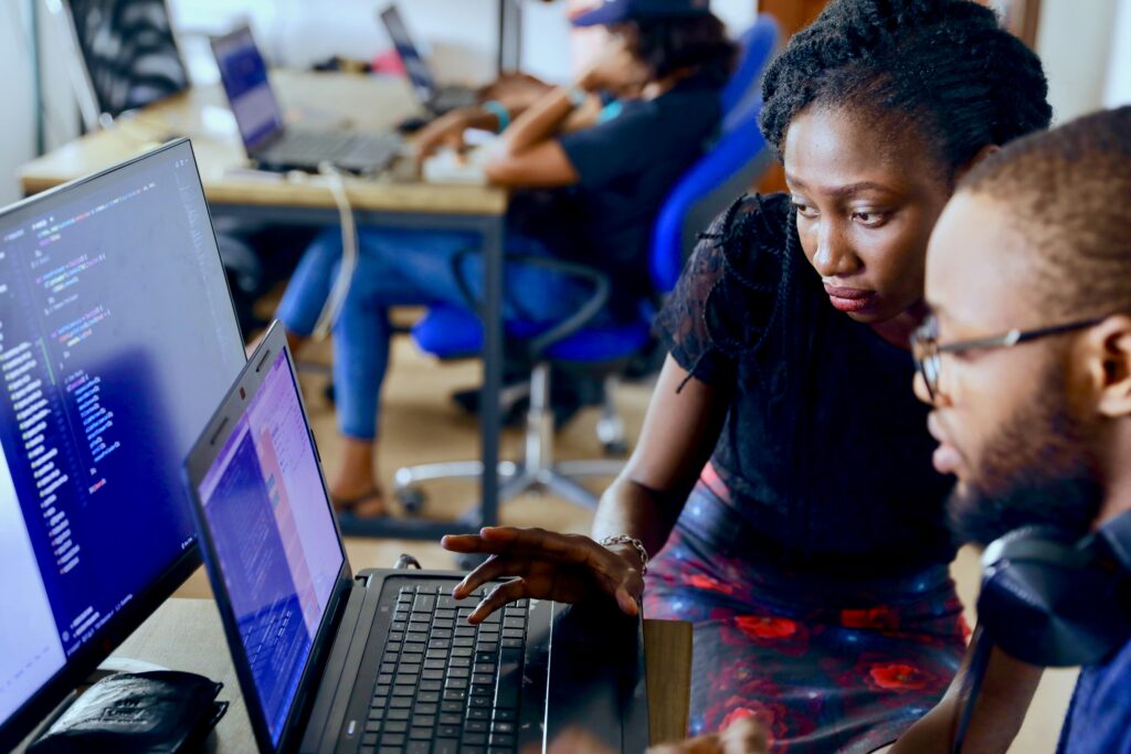 man and woman using laptop and looking at a screen with code on