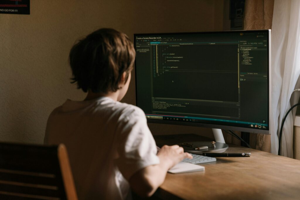 Coder sat in front of a desktop computer screen in a sparse home office